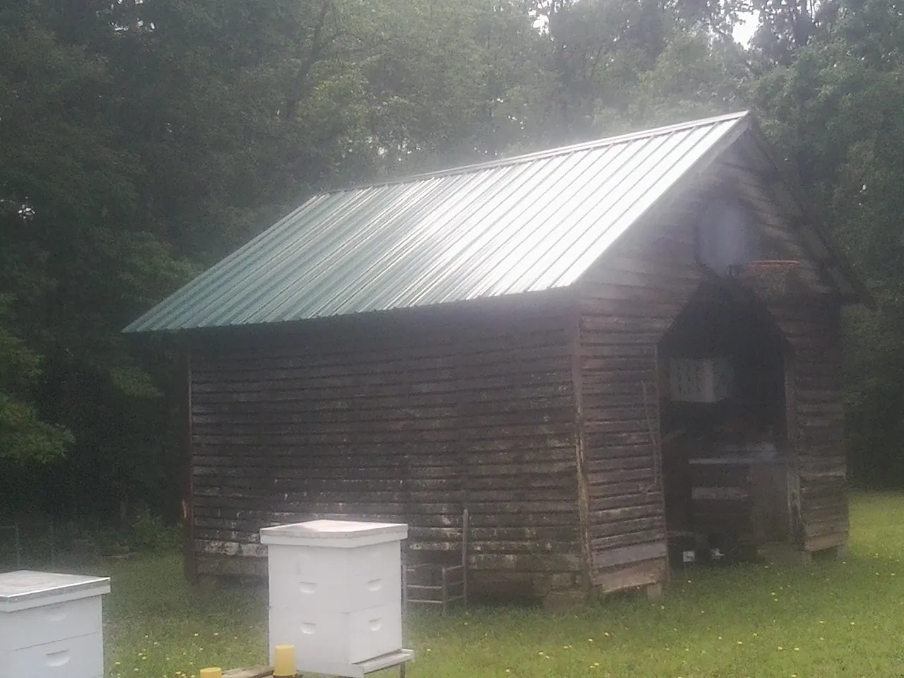 Green metal roof on a weathered barn beside stacked beehives in Cherry Valley