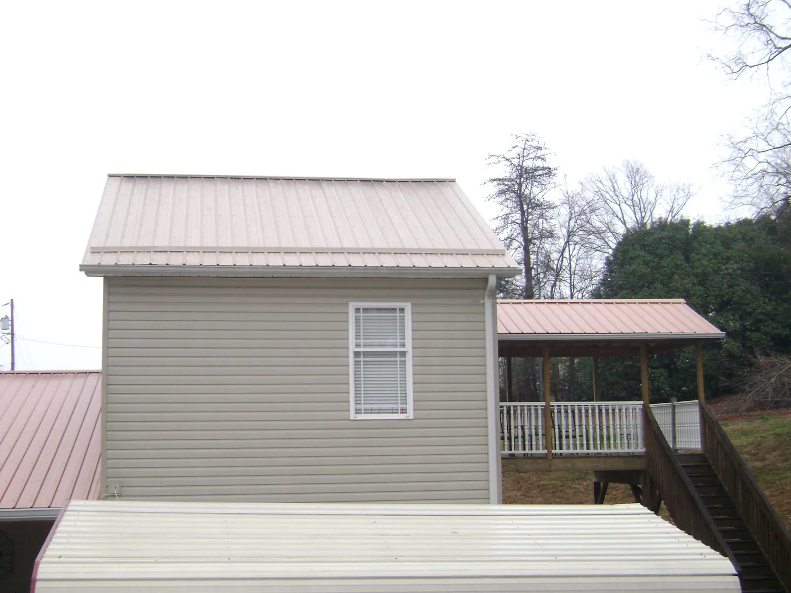 Tan metal roofs on a two story addition and attached porch, from a Roof Replacement job in Cherry Valley